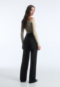 Top beige a coste con spalline scoperte abbinato a pantaloni neri a vita alta e gamba larga, caratterizzati da una texture liscia e un design minimalista.