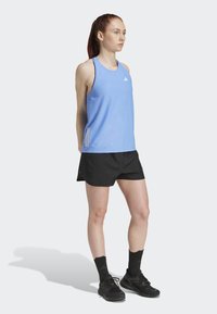 Atletische outfit met een lichtblauw mouwloos top met een Adidas-logo, zwarte shorts en zwarte hardloopschoenen met gestreepte sokken.