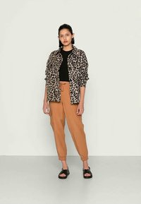 Camisa com estampado de leopardo, top preto, calças cargo cor caramelo e sandálias pretas. A camisa tem mangas dobradas e um corte descontraído. As calças têm uma cintura com cordão.