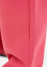 Gros plan d'un pantalon en tissu rose montrant la texture et le détail de la couture près de la cheville.