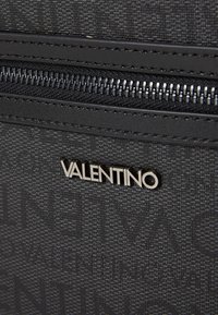 Sac à main en tissu noir texturé, avec fermeture éclair, logo Valentino en argent et coutures contrastées le long des bords.