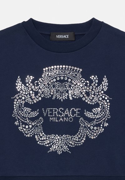 Svetlo modrá mikina s centrálnym strieborným dizajnom z kamienkov a textom "VERSACE MILANO", okrúhly výstrih a mäkká textúra látky.