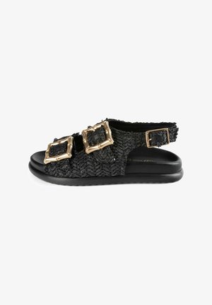 Schwarze geflochtene Flachsandalen mit zwei goldenen quadratischen Schnallen. Sie verfügen über ein strukturiertes Obermaterial und eine glatte schwarze Sohle. Offenes Rückendesign mit verstellbarem Riemen.