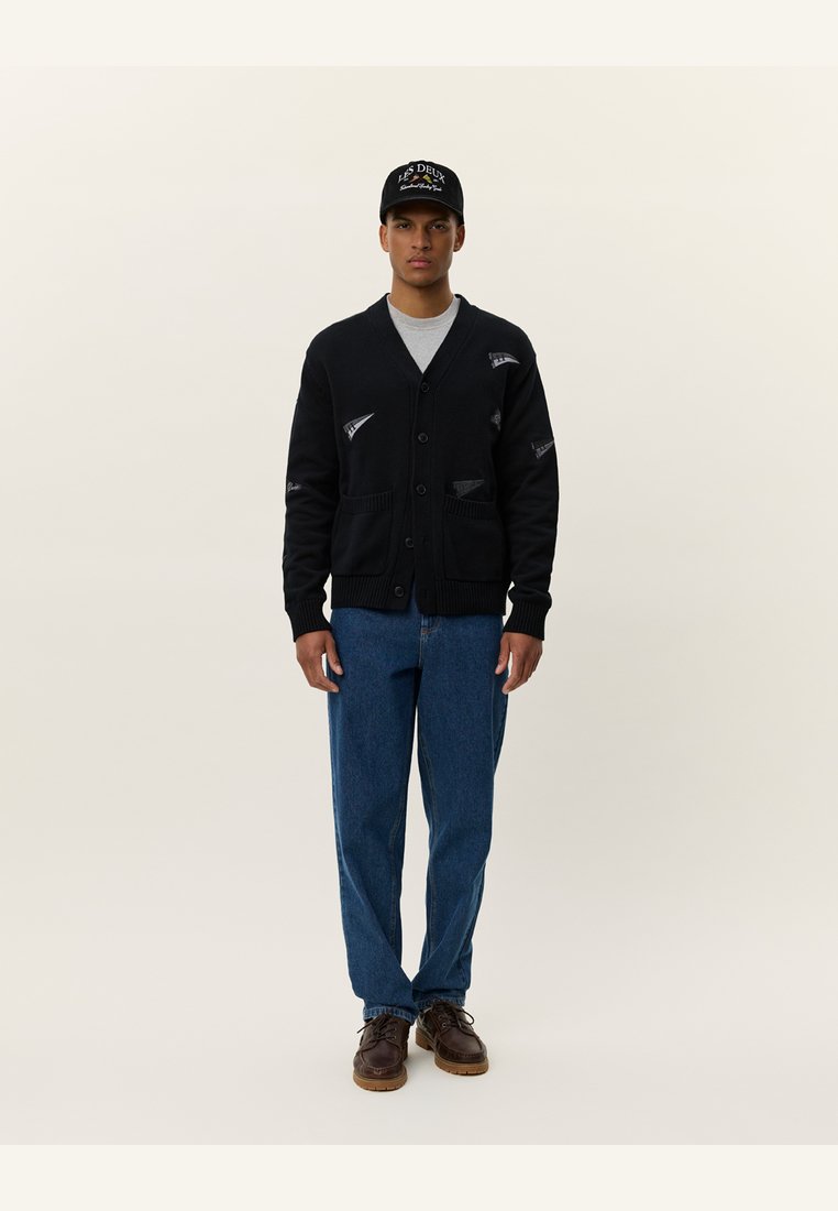 Cardigan negru cu închidere cu nasturi, două buzunare frontale și accente cu logo. Purtați peste o cămașă gri, cu blugi albaștri și pantofi maro. Design simplu.