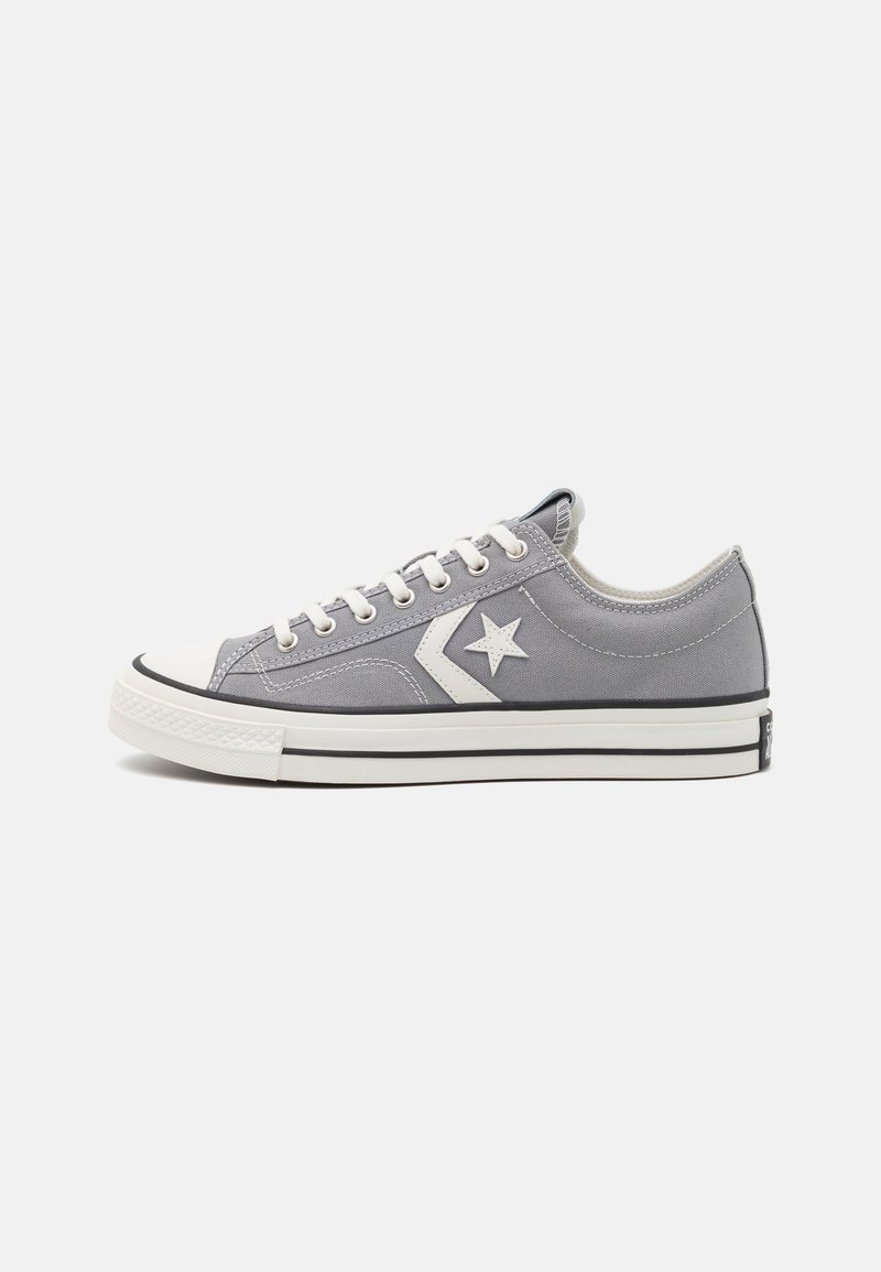 Baskets basses en toile grises avec lacets blancs, logo étoile blanc sur le côté et semelle en caoutchouc blanche avec une bande noire.