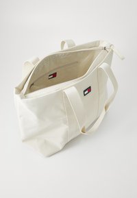 Beige nailonist kott, kahe kangast käepideme, lukuga sulgemise, sisepocketi ja väikese logo plaadiga, millel on punased, valged ja sinised värvid.