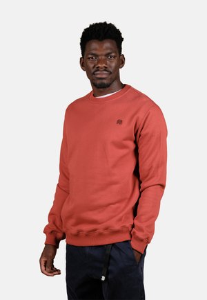 Sudadera de color coral con mangas largas, puños y dobladillo de canalé, que presenta un pequeño logo en el pecho. Fabricada con un tejido suave y texturizado.