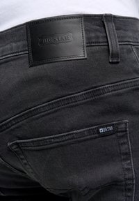 Jeans de mezclilla negra con un acabado texturizado y un parche prominente que presenta el logo "BIG STAR". Incluye dos bolsillos traseros con detalles de costura.
