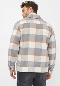 Veste à carreaux en tons de gris, crème et beige. Fabriquée en tissu texturé avec un col et des boutons en décoration. Présente une coupe décontractée et ample.