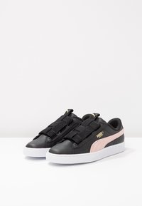 Baskets en cuir noir avec des accents roses, dotées d'une sangle élastique noire texturée, d'une semelle en caoutchouc blanc et d'un détail de logo doré.
