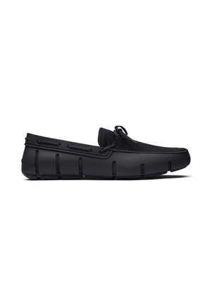 Zwarte mocassinschoen met gestructureerde stoffen bovenkant, veterdetail en gesegmenteerde rubberen zool, zijaanzicht op witte achtergrond.