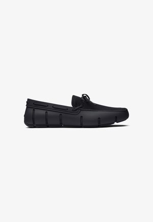 Zwarte mocassinschoen met gestructureerde stoffen bovenkant, veterdetail en gesegmenteerde rubberen zool, zijaanzicht op witte achtergrond.