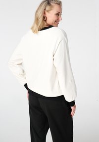 Roomwitte trui met zwarte geribbelde manchetten en zoom, met lange mouwen en een ontspannen pasvorm, getoond vanaf de achterkant.