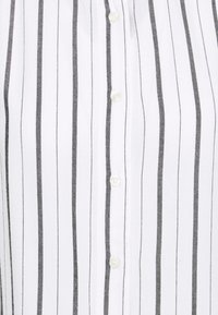 Camicia bianca con strisce verticali nere sottili, con colletto e cinque bottoni rotondi lungo la parte anteriore.