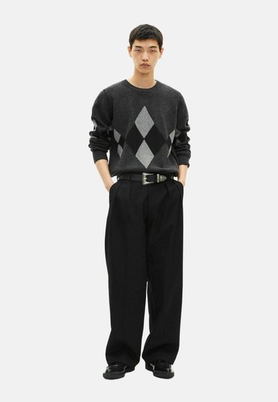 Suéter gris con patrón argyle negro y plateado, combinado con pantalones de pierna ancha negros y un cinturón negro con hebilla plateada. Zapatos negros.