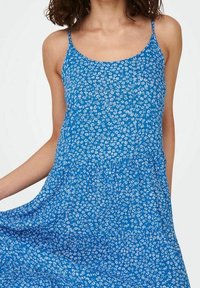 Sininen kukkamekko ohuilla olkaimilla, jossa on istuva yläosa ja levenevä hame. Materiaali on pehmeää ja siinä on toistuva pieni valkoinen kukkakuvio.