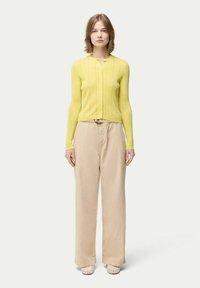 Gul ribbad stickad cardigan med rund halsringning, knappstängning och långa ärmar, tillsammans med ljusbeige vida byxor.