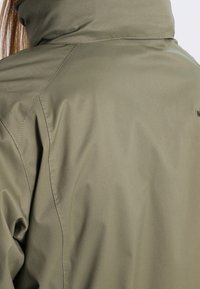 Olivegrüne wasserdichte Jacke mit hohem Kragen, glatter Textur und gesteppten Nähten. Verfügt über Branding auf der Rückseite und ein lässiges Schnittdesign.