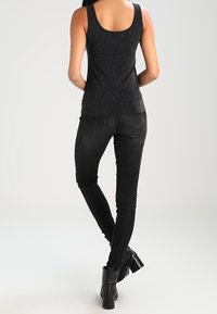 Žena v černém bezramínkovém topu se třpytkami, černých skinny džínách a černých kotníkových botách, stojí zády k fotoaparátu.