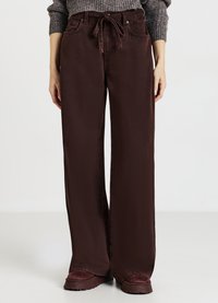 Pantaloni larghi bordeaux con coulisse, dotati di tasche anteriori e texture liscia. Abbinati a scarpe marroni chunky.