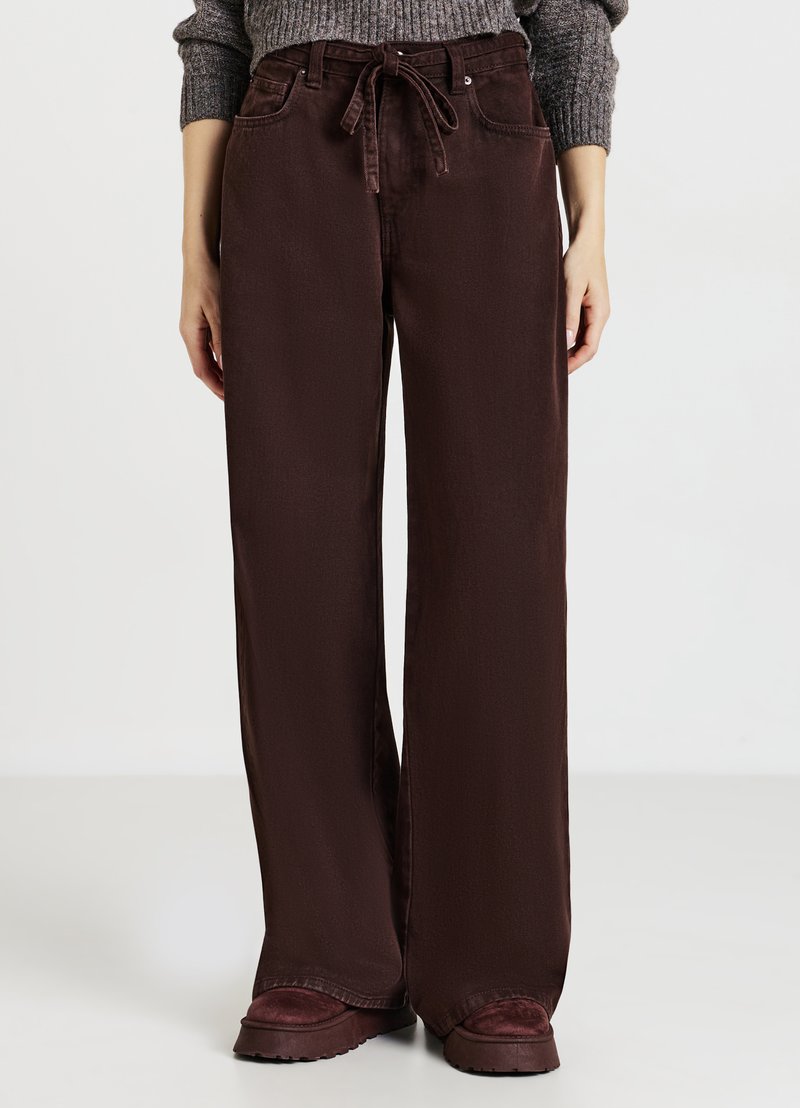 Pantaloni larghi bordeaux con coulisse, dotati di tasche anteriori e texture liscia. Abbinati a scarpe marroni chunky.