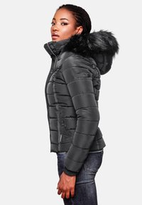 Black puffer jacket with a detachable faux fur hood, quilted design, zippered front, and side pockets. Worn with dark denim jeans.