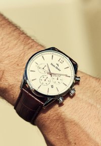 Silver chronograph watch with a white dial, brown leather strap, and three sub-dials. Features include a date function and polished hardware.