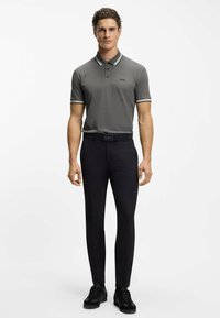 Szara koszulka polo z czarno-białymi paskami na kołnierzyku i rękawach, zestawiona z czarnymi dopasowanymi spodniami i czarnymi trampkami.