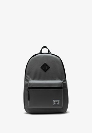 Sac à dos gris au design élégant, fabriqué en matériau durable, avec une poche avant zippée et un patch logo en forme de losange.