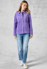 Violet kauffert jakke med to brystlommer, knaplukning og krave; parret med lyseblå løse jeans og hvide sneakers.