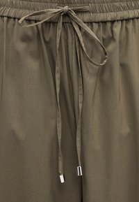 Παντελόνι με ελαστική μέση σε ελαιί πράσινο χρώμα, με δεμένο υφασμάτινο κορδόνι και ασημί μεταλλικά τελειώματα στις άκρες.