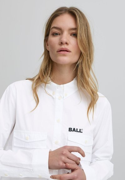 Weißes Hemd mit Knopfverschluss und Kragen sowie zwei Vordertaschen. Mit einem schwarzen "BALL"-Logo auf der linken Tasche. Aus Baumwollstoff, mit glatter Textur.