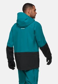 Türkisfarbene und schwarze wasserdichte Jacke mit Kapuze, langen Ärmeln und verstellbaren Bündchen. Verfügt über ein Logo auf dem Rücken und ein strukturiertes Material.