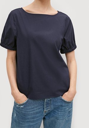 Haut bleu marine avec un décolleté bateau, manches courtes bouffantes avec élastique froncé, associé à un jean bleu clair déchiré.