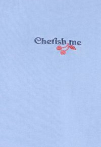 Lichtblauwe stof met donkerblauwe geborduurde tekst "Chefish me" naast een klein rood kersontwerp met twee kersen en een blad.