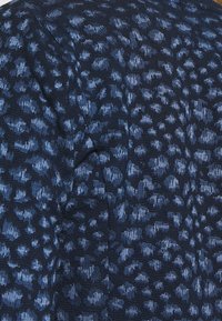 Tessuto a maglia blu navy con motivi astratti blu più chiaro. Superficie testurizzata con un'apparenza sottile e stratificata. Dettagli non specificati.