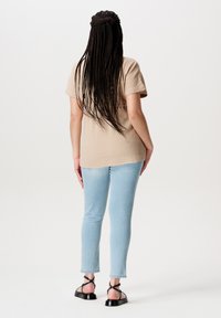 Beige strukturiertes T-Shirt mit kurzen Ärmeln, kombiniert mit hellblauen Slim-Jeans. Schwarze Riemchensandalen vervollständigen das Outfit.