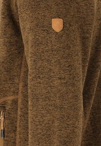 Giacca marrone con zip e tessuto testurizzato. Presenta una piccola toppa in pelle con logo e dettagli della cerniera visibili sul lato.