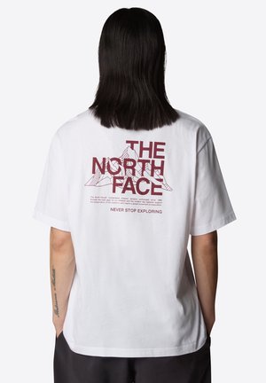 Personne aux cheveux foncés mi-longs portant un T-shirt blanc avec le logo "THE NORTH FACE", un graphisme de montagne et le texte "NEVER STOP EXPLORING" au dos.