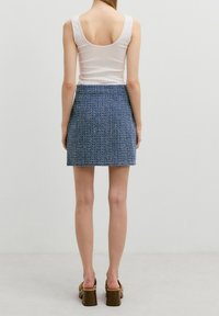 Een witte tanktop gecombineerd met een gestructureerde blauwe minirok, met een aansluitende pasvorm. De persoon draagt bruine platformhakken.