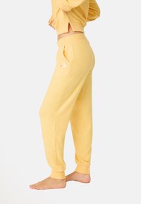 Pantaloni della tuta gialli realizzati in morbido tessuto, con una vestibilità comoda, vita elastica, tasche e ricamo floreale sulla tasca sinistra.