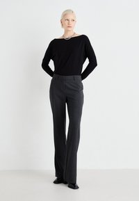 Black long-sleeve top with an open neckline, paired with high-waisted, tailored grey slacks and black heeled shoes. Simple, clean design.