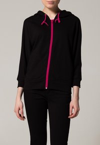 Felpa nera con zip rosa e stringhe, realizzata in un tessuto morbido, con tasche frontali e una vestibilità comoda.