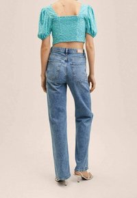 Blaue Jeans aus Denim mit geradem Schnitt, kombiniert mit einem verkürzten, puffärmeligen, türkisfarbenen Oberteil mit floralem Muster. Glatte Textur.