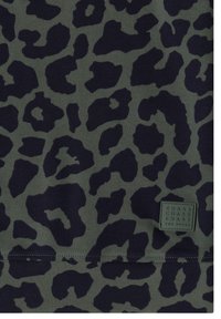 Tissu vert foncé avec des taches noires irrégulières de léopard et une petite étiquette carrée cousue indiquant "CHASE THE PULSE" dans le coin inférieur droit.