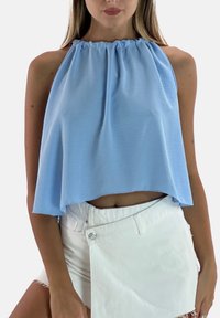 Top a fascia azzurro chiaro con scollo arricciato, tessuto fluente e design ampio e corto. Abbinato a pantaloncini di jeans bianchi.