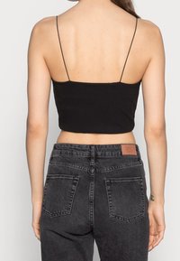 Haut court côtelé noir à fines bretelles, associé à un jean en denim gris foncé taille haute avec une pièce patch et deux poches arrière.