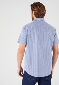 Camicia a maniche corte a quadri in cotone blu e bianco, con colletto button-down e orlo curvo. Cuciture visibili sulle spalle.
