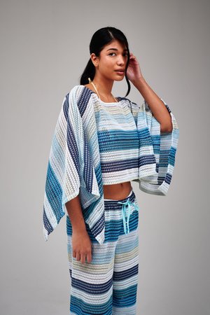 Młoda kobieta pozująca w niebieskim, białym i beżowym swetrze w paski o szerokich rękawach oraz dopasowanych spodniach z ściągaczem w pasie.