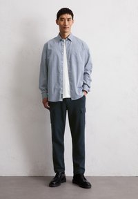 Chemise à carreaux bleu clair par-dessus un t-shirt blanc, accompagnée de pantalons cargo vert foncé et de bottes noires à lacets.